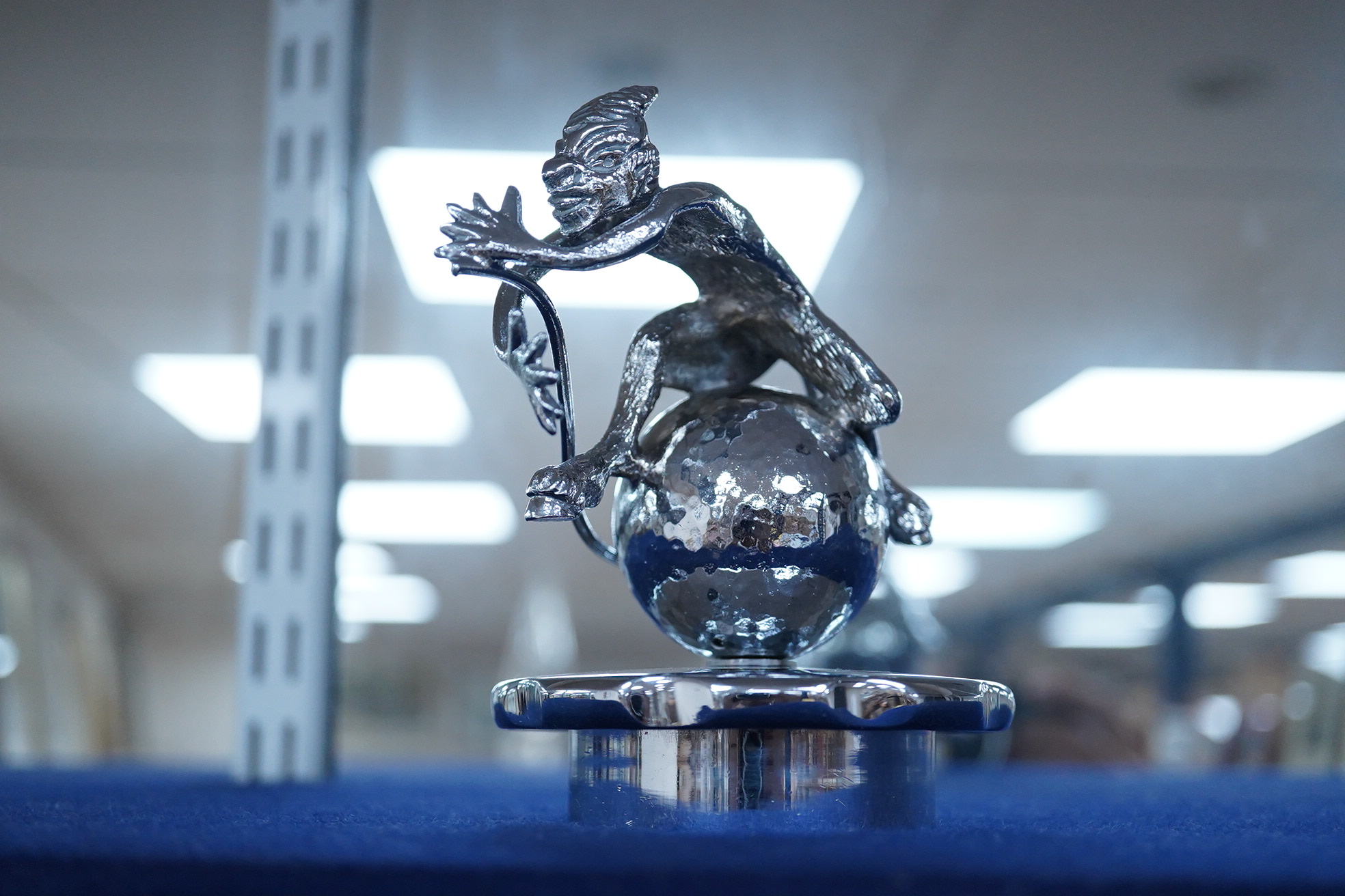 Six chrome and brass car mascots, including; a figure with a dolphin, a figure of Cupid, a grotesque in the form of a devil, a figure of a Tudor gentleman, an Art Deco figure of a flying woman, etc.